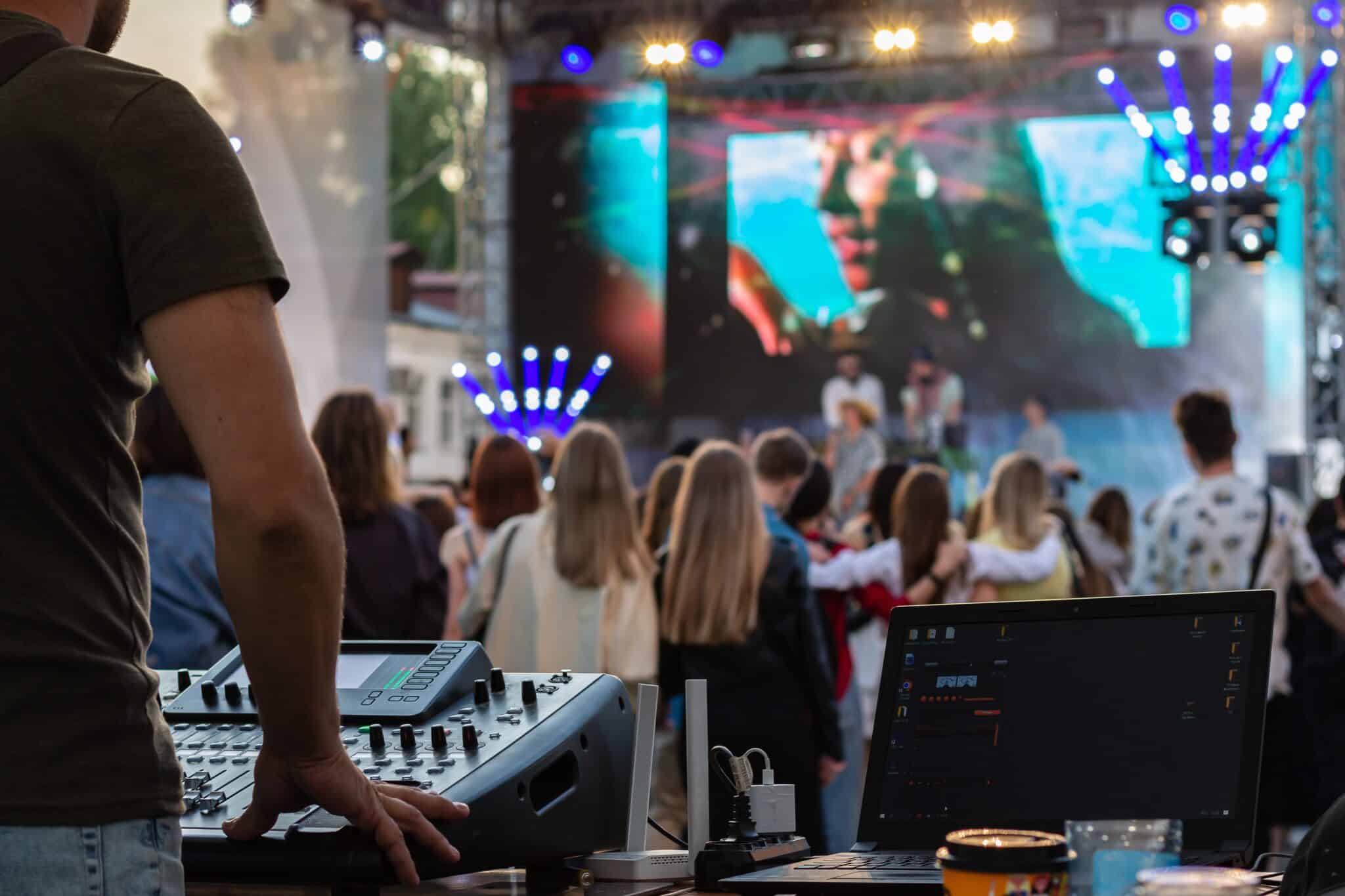 low light, professional DJ music mixer, laptop at party festival with crowd of people in background